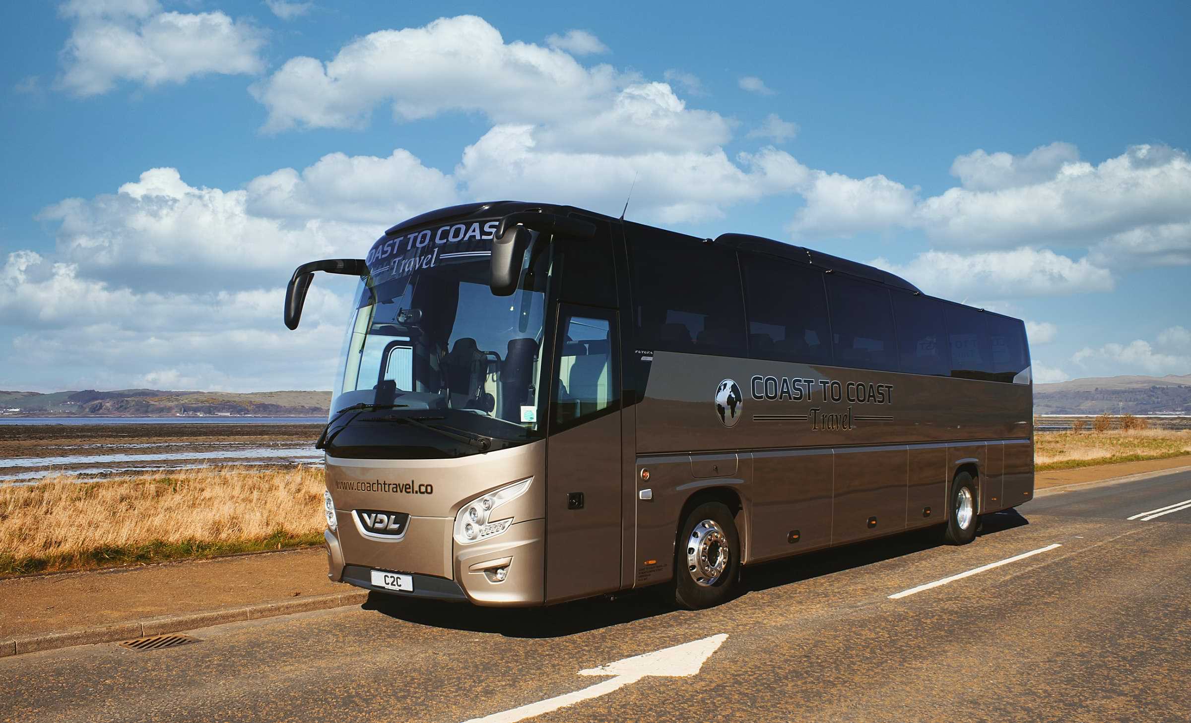 Side view of Coast to Coast Travel coach, parked at the roadside with some low hills in the background