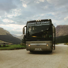 Two Coast to Coast Travel coaches parked in a gravelled space in the Highlands, with a view of some mountains in the distance
