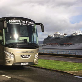 Side view of a Coast to Coast Travel coach parked at the coast, with a large cruise ship on the water in the background