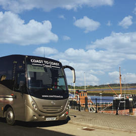 Coast to Coast Travel coach parked next to the coastline with some boats on the water in the background